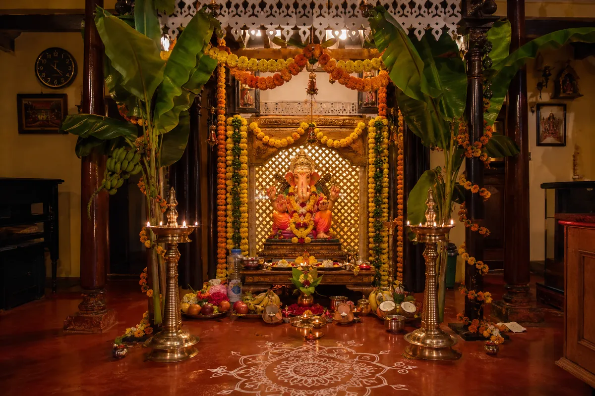 Decorated Ganpati idol with marigold garlands and brass lamps at a traditional Konkan village home during Ganesh Utsav